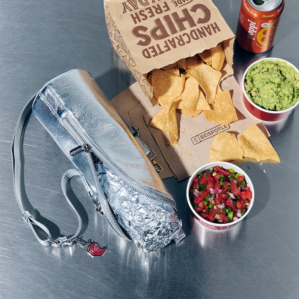A silver, insulated bag with a pepper charm next to a Chipotle chips bag, guacamole, salsa, and a Poppi soda.