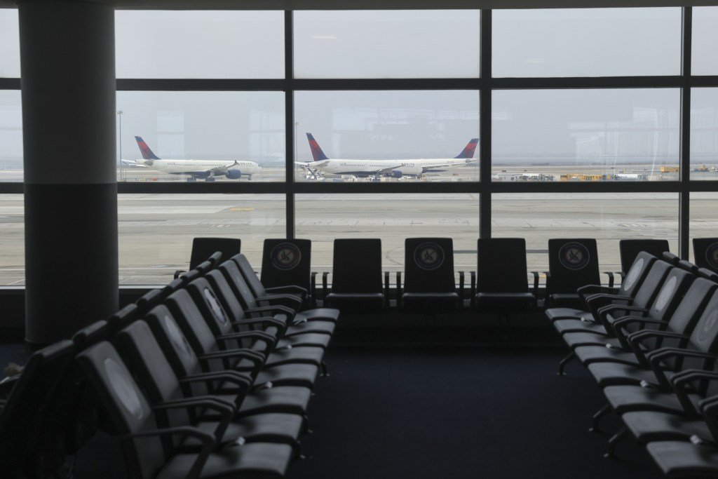 View of airplanes on the tarmac from an airport waiting area with empty seats marked for social distancing.