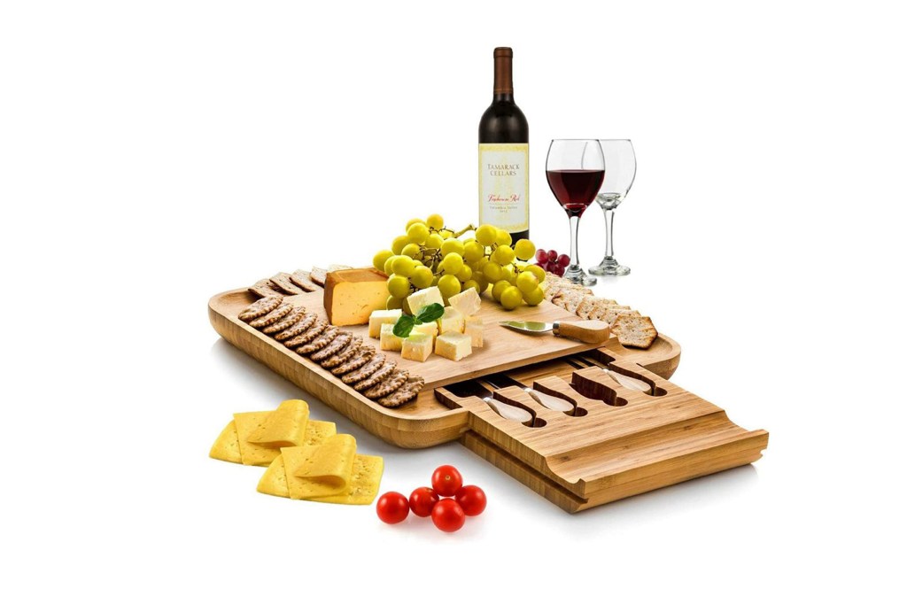 Bamboo cheese board with cheese, crackers, grapes, and wine.