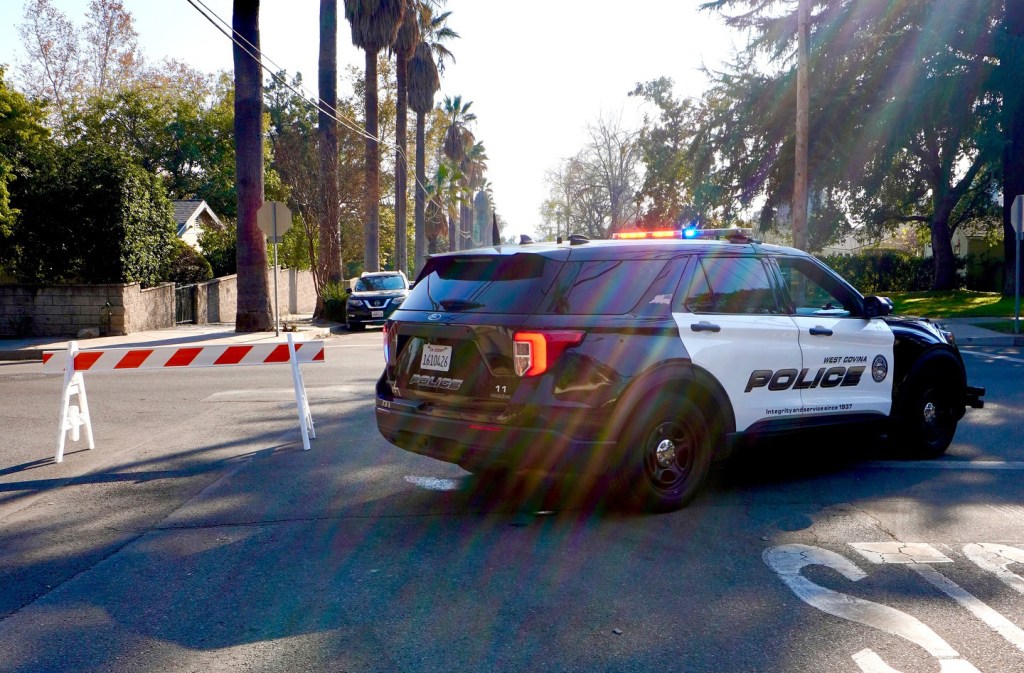 West Covina Police Department car with flashing lights and a road barrier.