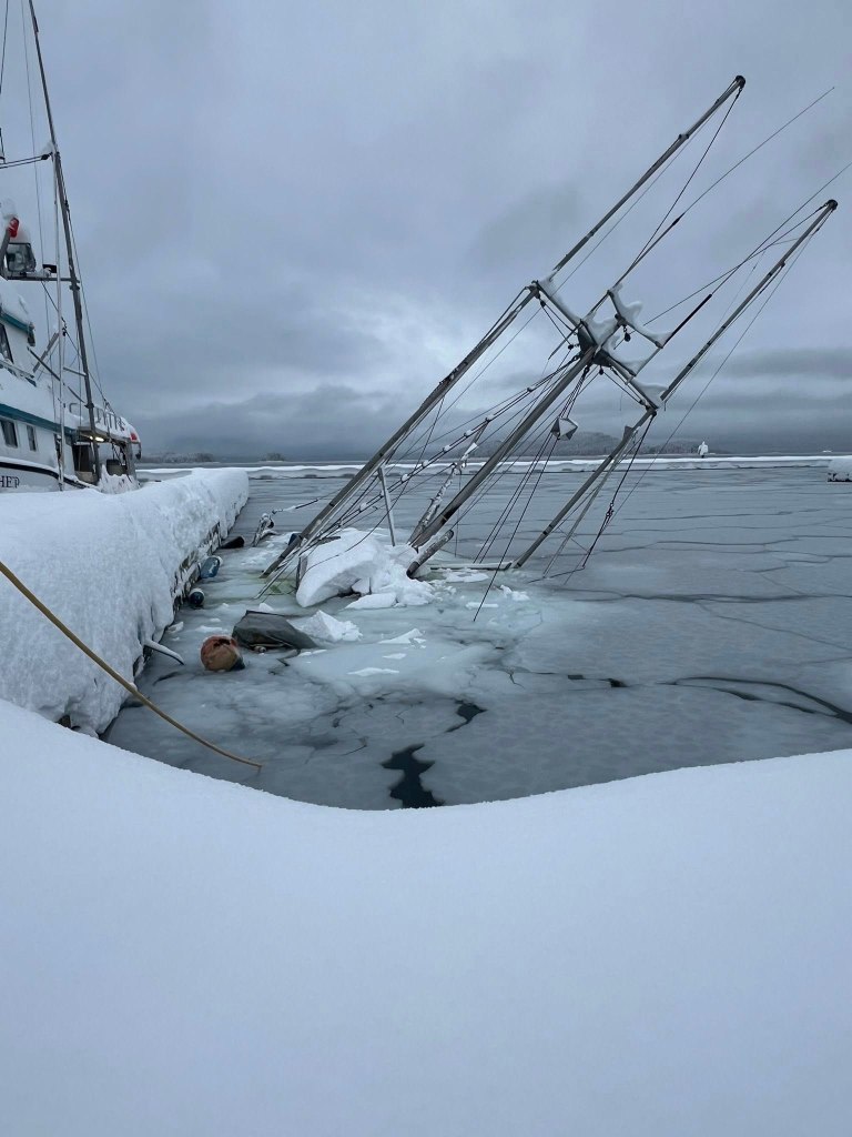 A sunken boat in a frozen harbor, with its masts angled into the icy water.
