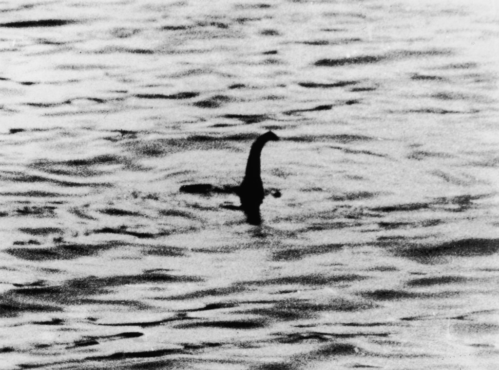 Black and white photograph of the Loch Ness Monster with its long neck and head visible above choppy water.