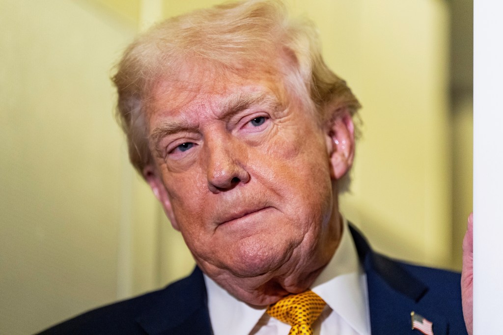 President Donald Trump, in a dark suit and yellow tie, listens intently to reporters while in flight on Air Force One.