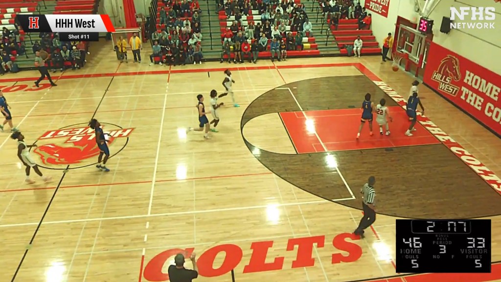 A high-angle view of a basketball game in progress, showing several players on the court and spectators in the stands.