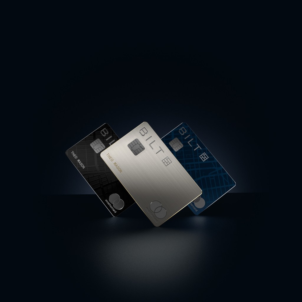 Three Bilt credit cards in black, silver, and blue, fanned out against a dark background.