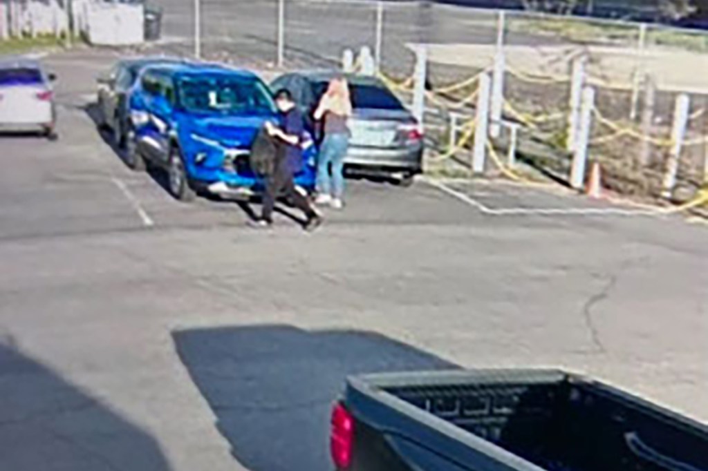 Two people walking past a blue SUV in a parking lot.