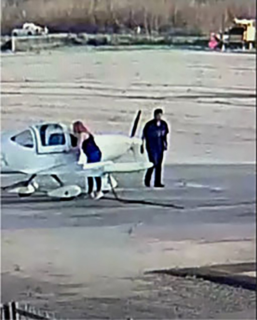 Two people next to a small white airplane on an airfield.