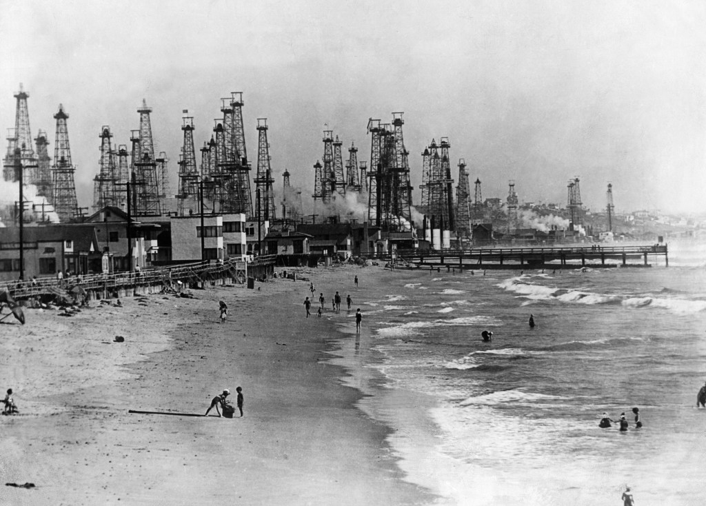 Oil derricks along Venice Beach, with people on the shore and in the water.