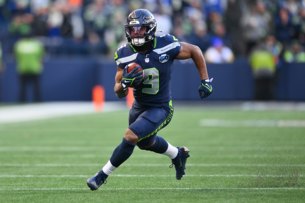 A Seattle Seahawks player in a dark blue uniform running with the football during a game.