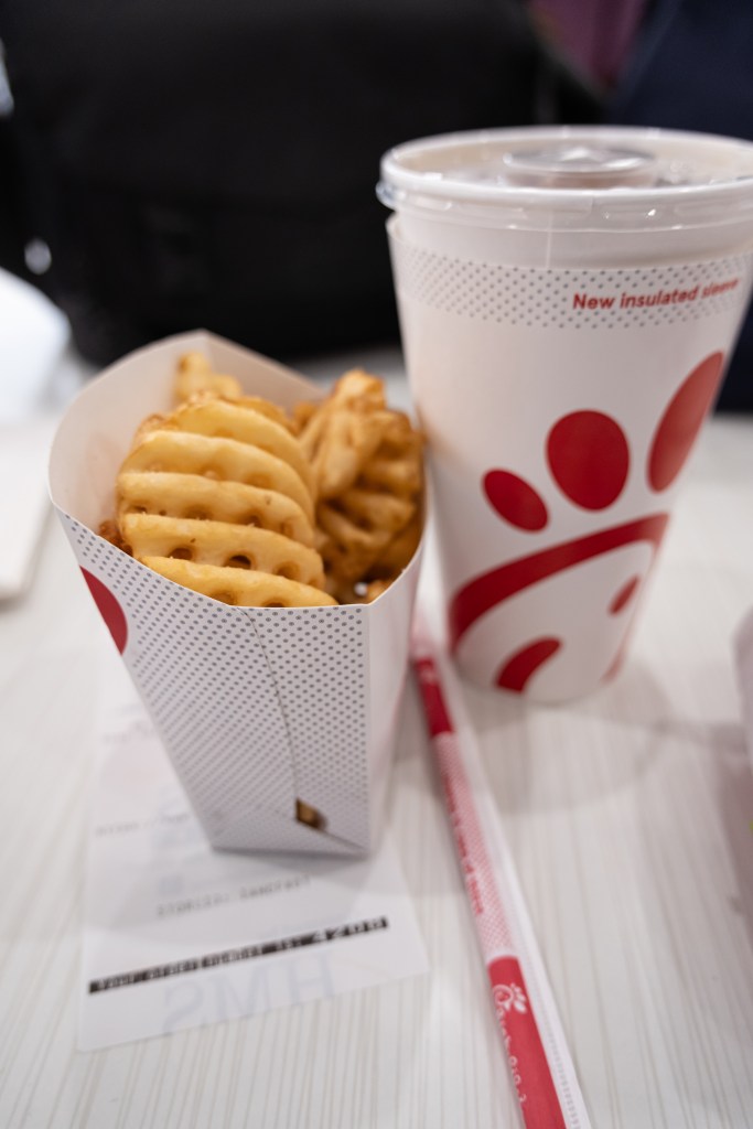 A Chick-fil-A meal with waffle fries and a drink with a "New insulated sleeve" on a white table.