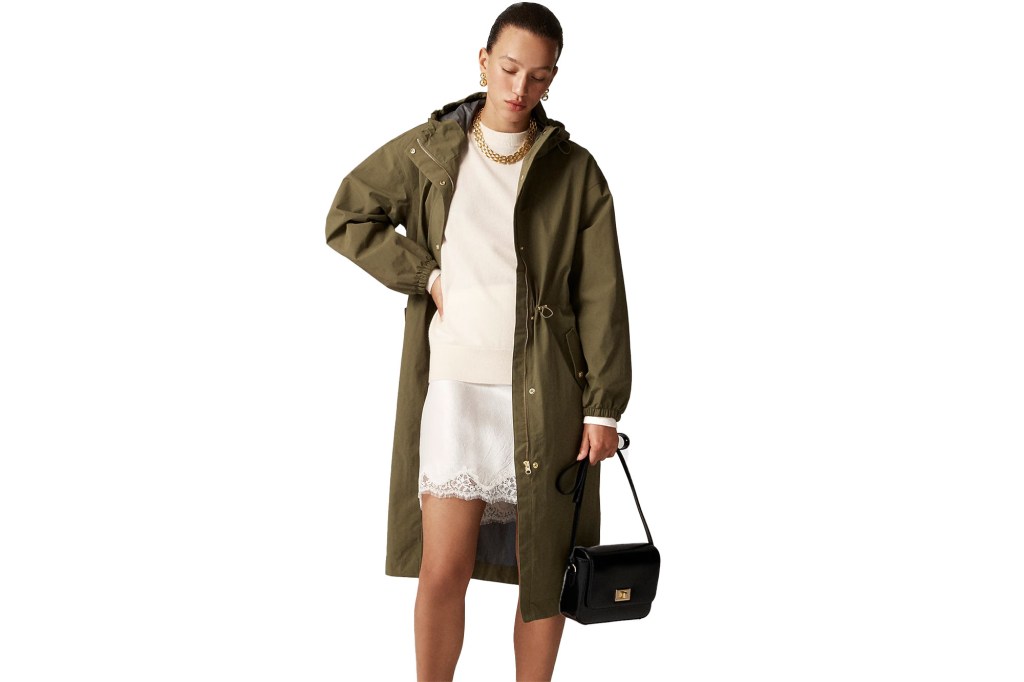 A woman models a J.Crew coat, wearing a white sweatshirt and skirt with a military green overcoat and black handbag.