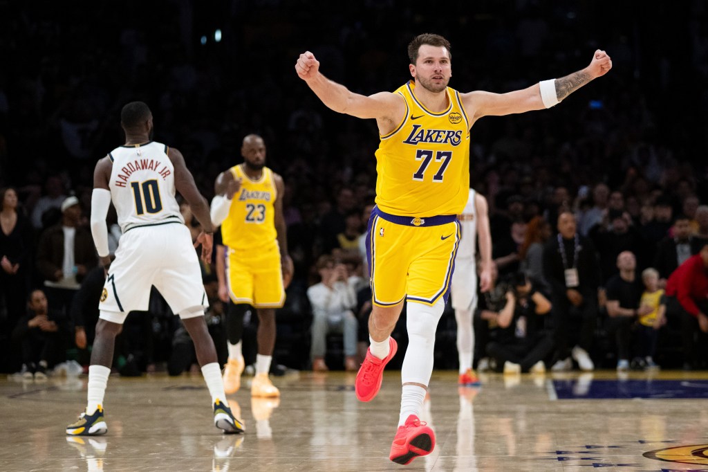 Luka Dončić, wearing a yellow Lakers jersey with number 77, gestures with both arms raised in celebration on the basketball court.