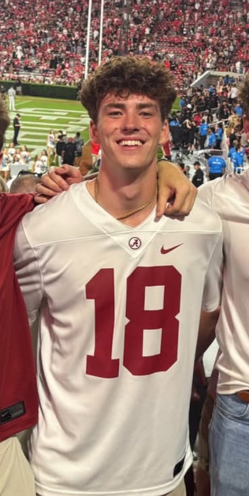 James “Jimmy” Gracey, a smiling University of Alabama student, wearing a white jersey with the number 18, is shown at a football game.