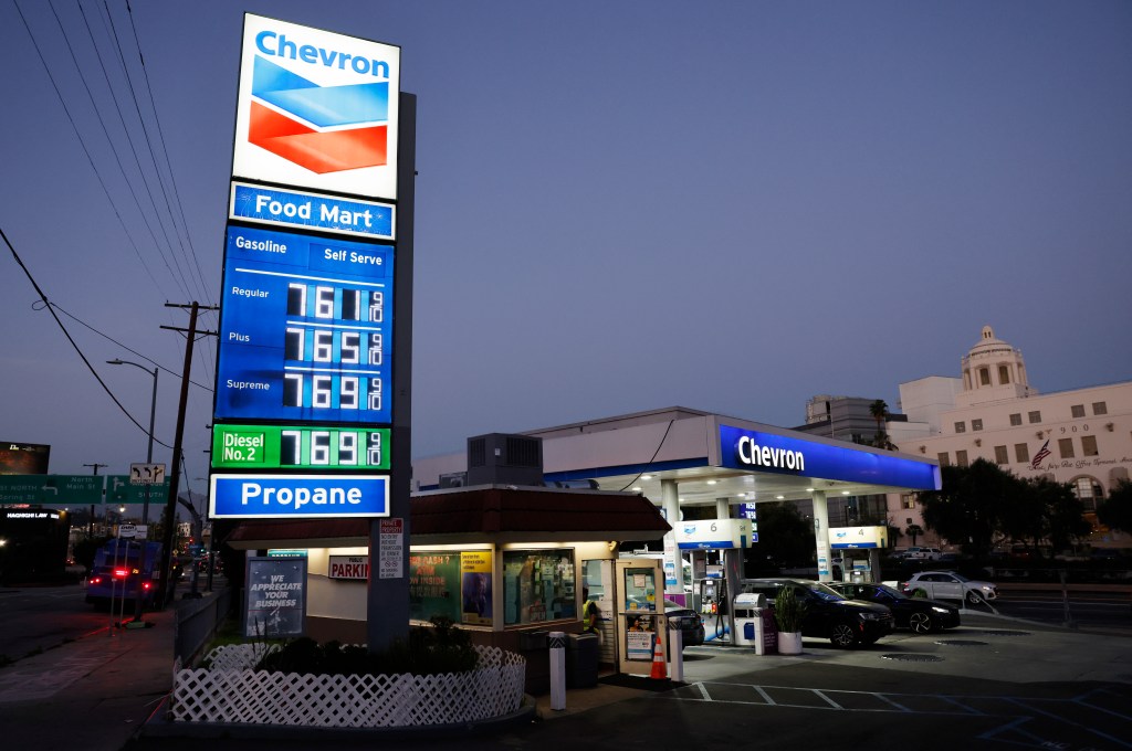 A Chevron gas station at dusk shows gas prices at $7.61 for regular, $7.65 for plus, and $7.69 for supreme gasoline, with diesel and propane also listed.