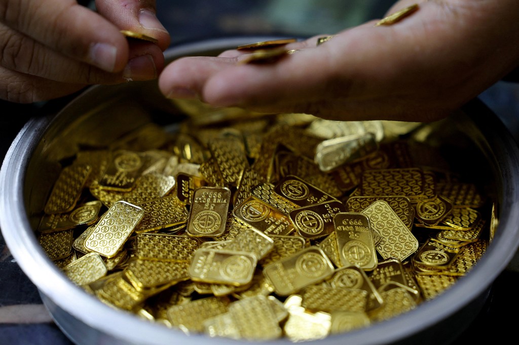 A hand places a small gold bar into a container full of various gold bars and pieces.