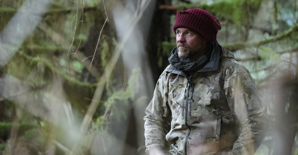 Paul Preece from Outlast in a red beanie and camouflage jacket in a forest.