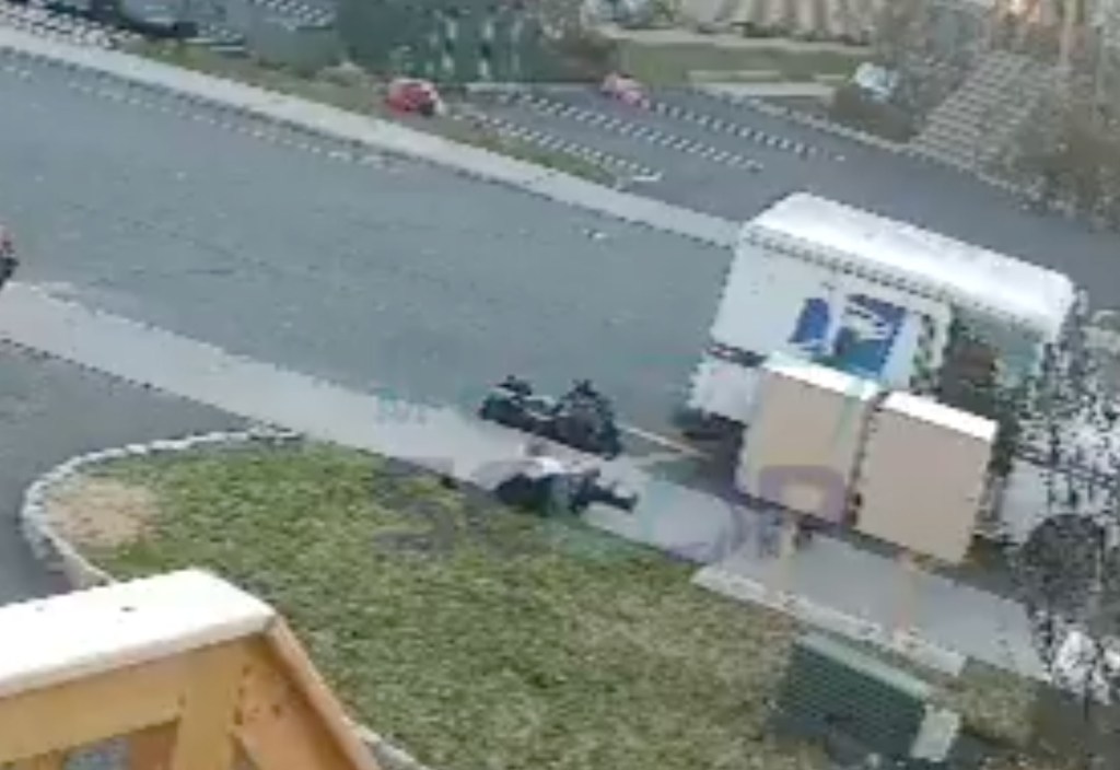 A postal worker shoves a child to the ground next to a postal truck.