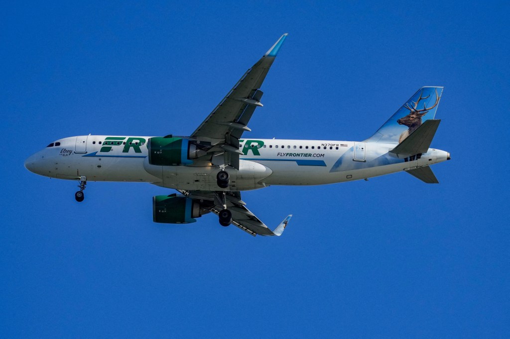 A Frontier Airlines plane with a large elk painted on its tail, against a clear blue sky.