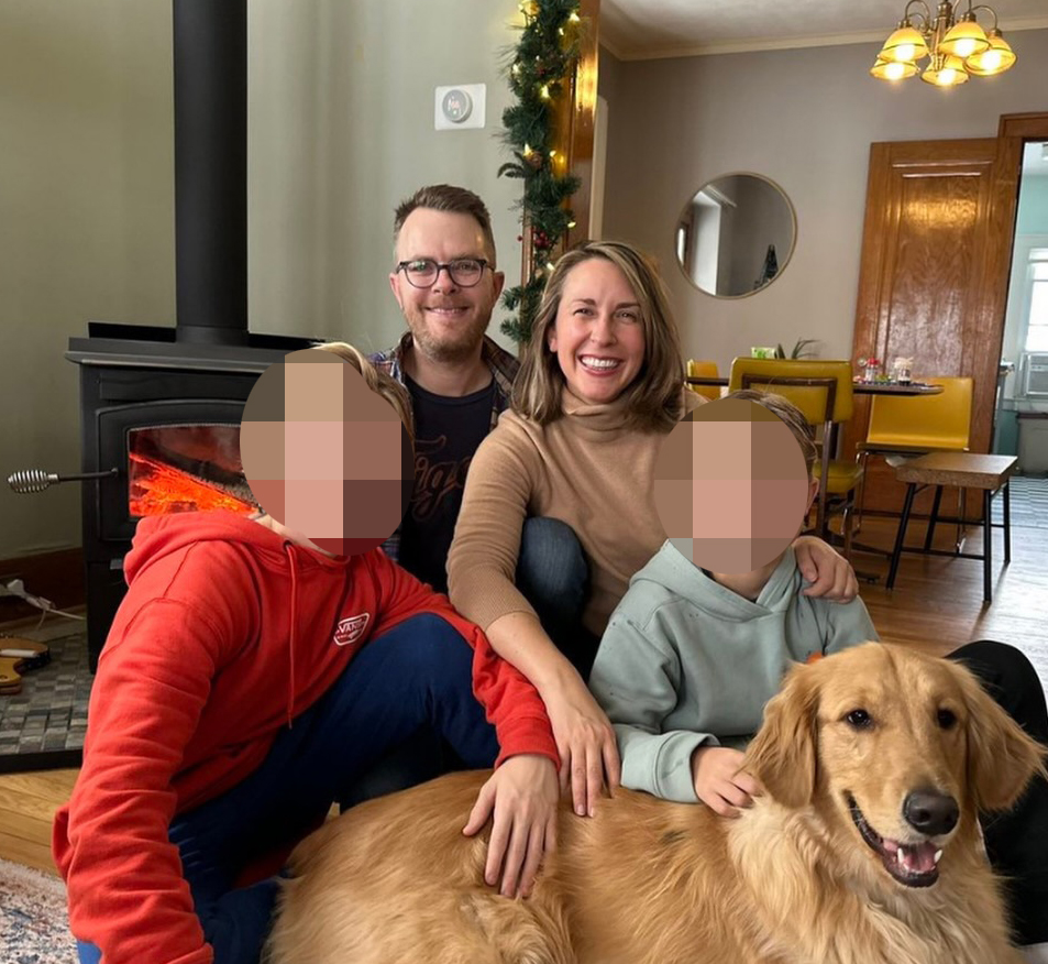 A family with two children and a golden retriever sits in front of a fireplace.