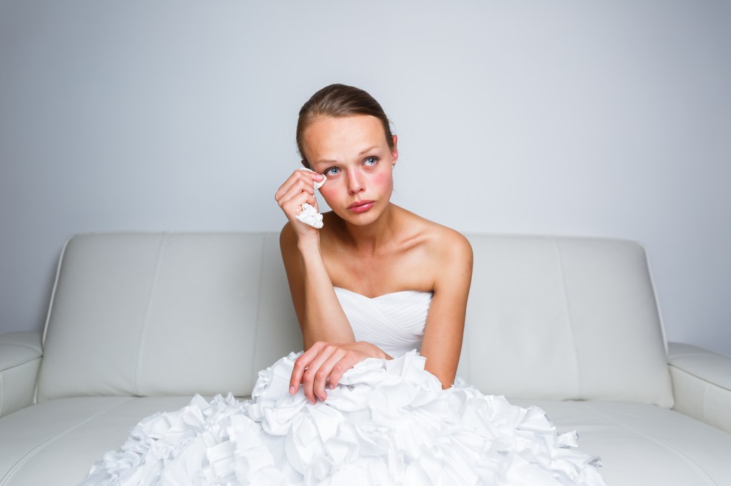 Sad bride crying while sitting on a white couch.