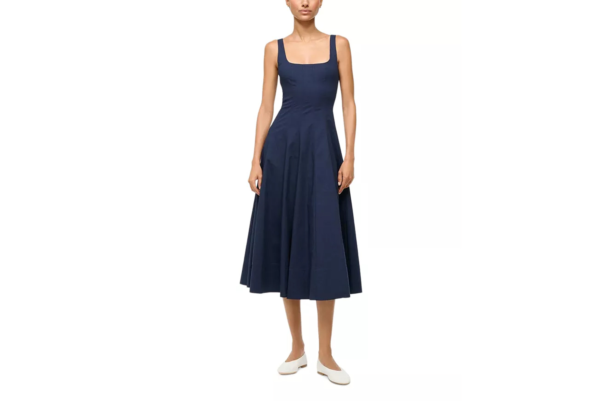 A model wears a navy blue Staud Wells dress with white flats.
