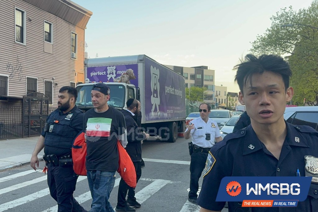 Two police officers and other men on a street in Brooklyn, with a "perfect moving" truck in the background.