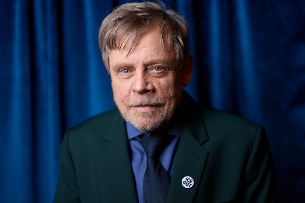 Mark Hamill poses for a photo wearing a suit and a lapel pin that says "ICE OUT".