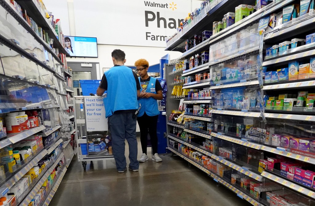 Two Walmart employees restocking shelves in the pharmacy section.