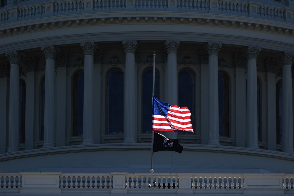 An American flag and POW/MIA flag fly at half-staff in front of the U.S. Capitol building.