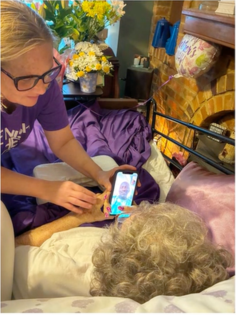 A woman helping an elderly person lying in bed video call a man.