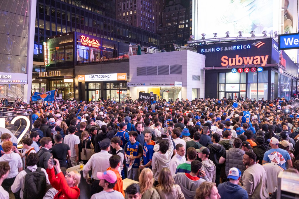 A large crowd of Knicks fans gathered and celebrated a victory in a street filled with shops and subway entrances.