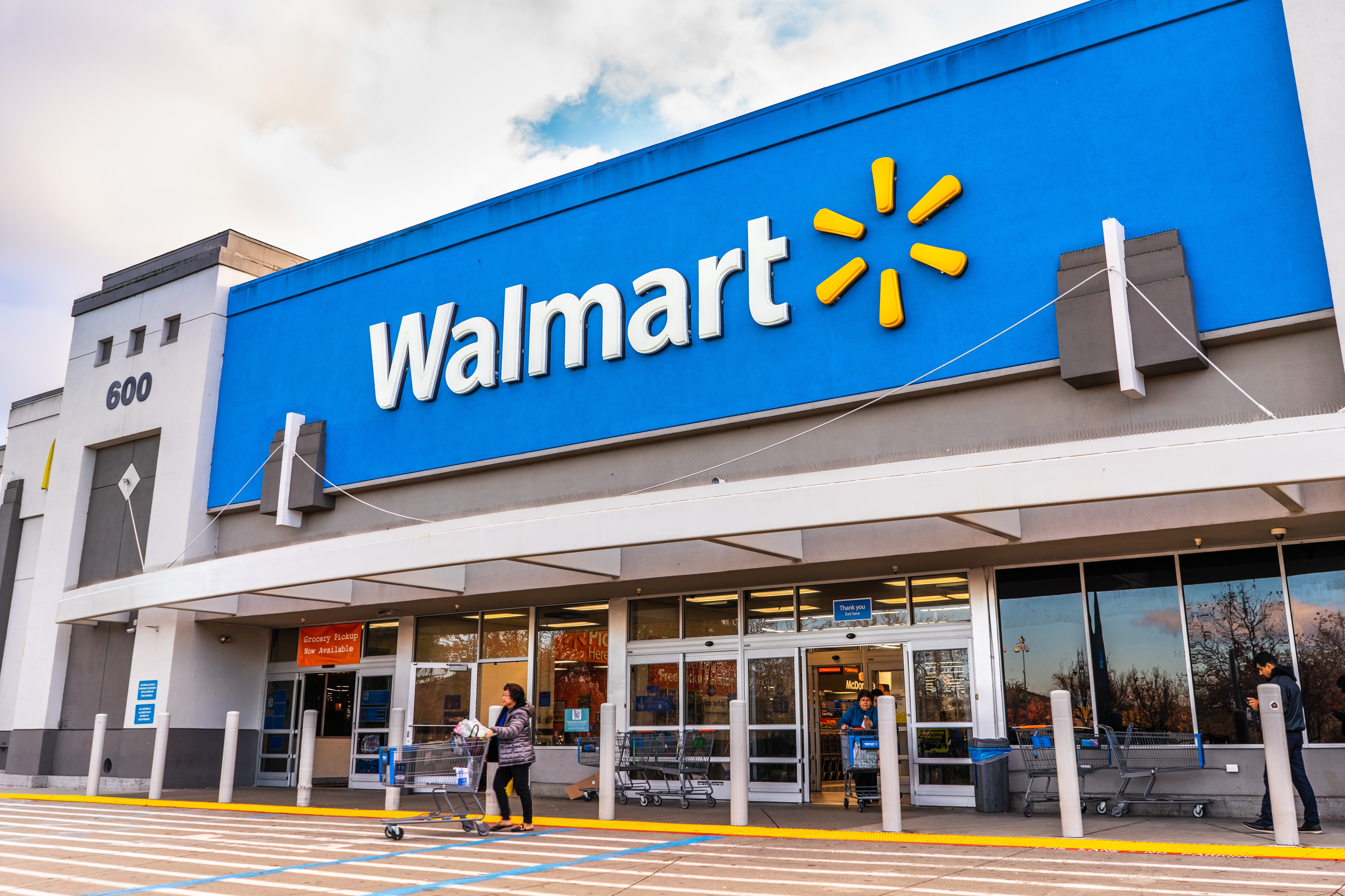 Exterior view of a Walmart store with its blue and yellow logo, and shoppers entering and exiting.