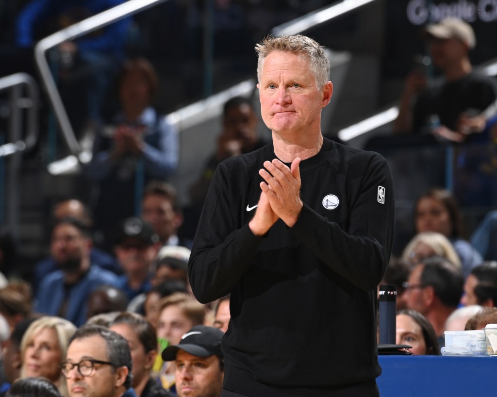 Basketball coach Steve Kerr clapping on the sidelines during a game between the Houston Rockets and Golden State Warriors.