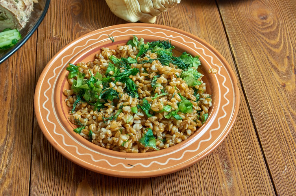 A close-up of Triple Herb Freekeh, an ancient grain dish, served in an earthenware bowl with a white wavy pattern along the rim.